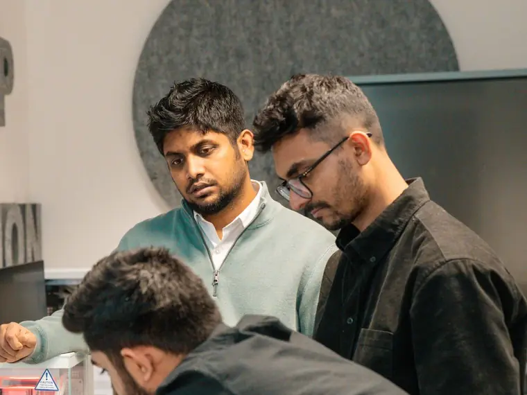 A senior engineer guiding two younger engineers at a workstation